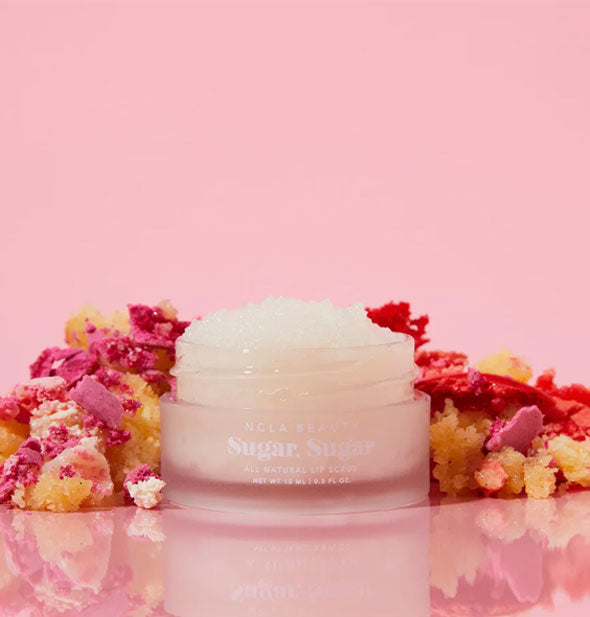 Pot of whitish NCLA Beauty Sugar, Sugar All Natural Lip Scrub is flanked by colorful, crumbly pieces of birthday cake