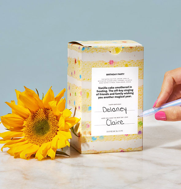 Model writes To and From designations on the Birthday Party candle box, staged with a sunflower