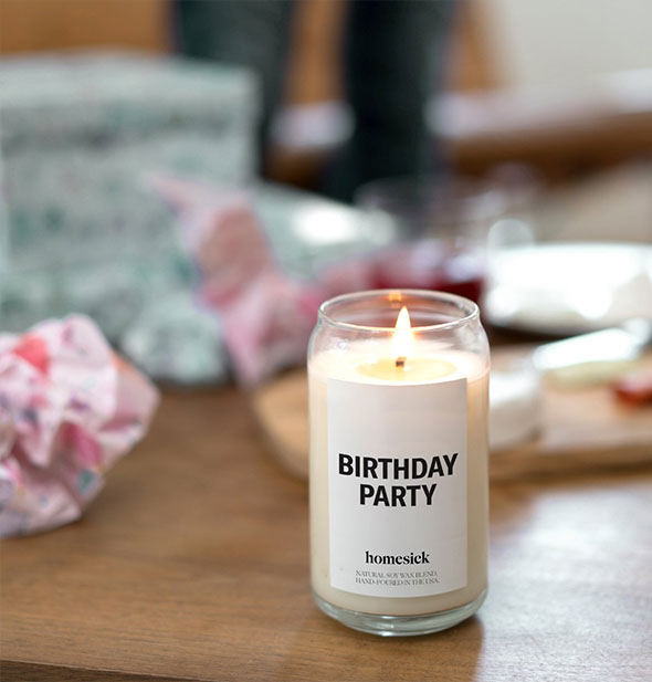 A lit Birthday Party candle on wooden tabletop with wrapped gifts in the background