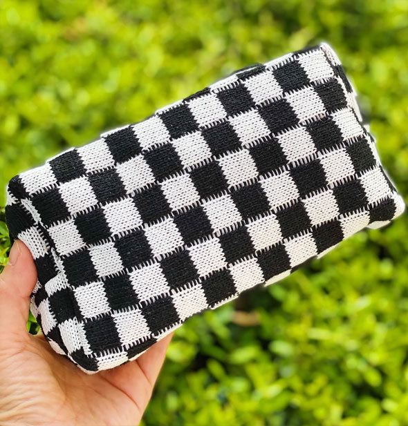 Model's hand holds a black and white checker print knit makeup bag