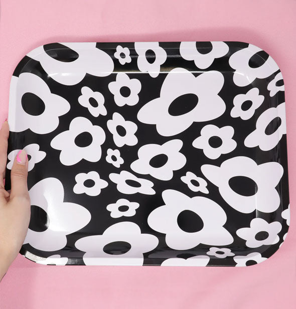 Model's hand holds the side of a black and white flower print tray for size reference