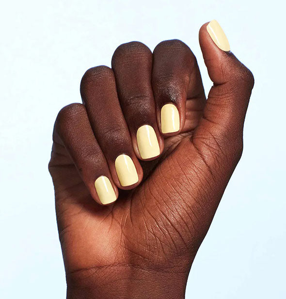 Model's hand wears a pale shade of yellow nail polish