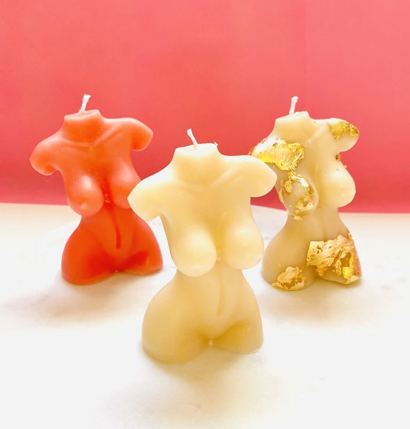 Grouping of three nude torso candles in pink, white, and gold leaf