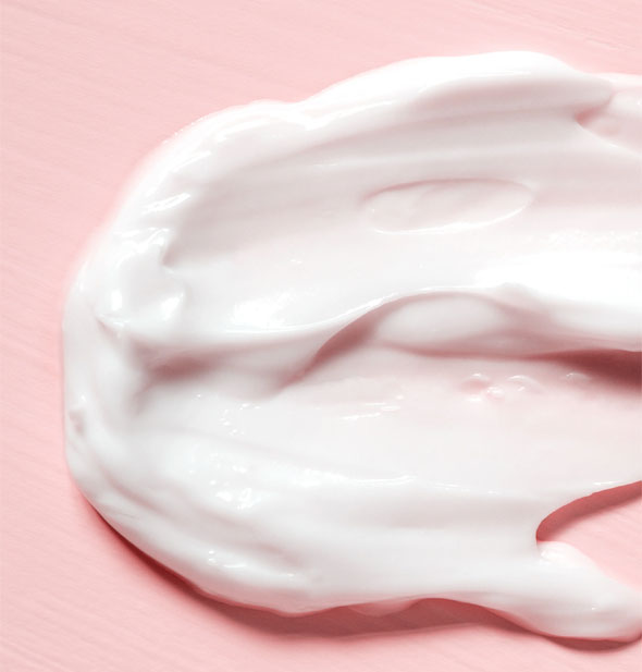Closeup of thick, white moisturizer cream on a pink surface