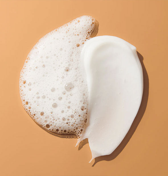 White, frothy shampoo and white, creamy conditioner applications on an orange surface