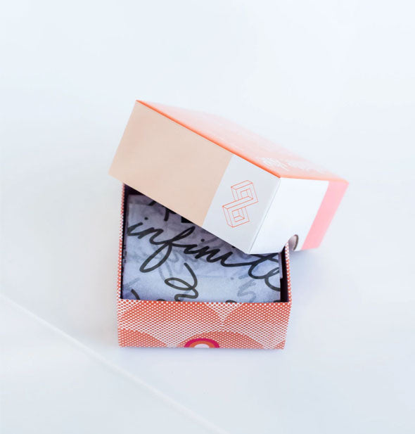 Decorative orange box with lid partially removed shows black and white handwritten pattern tissue paper inside