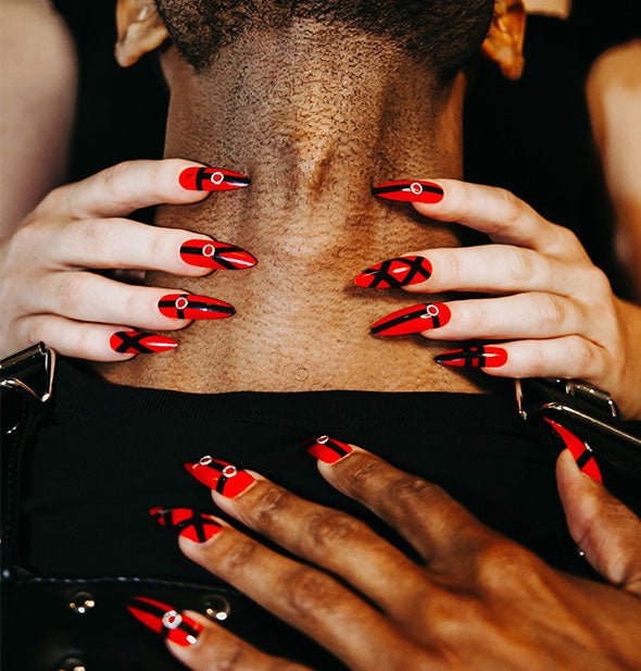 Models wearing red and black Bondage Nailz pose together, one with hands around the other's neck