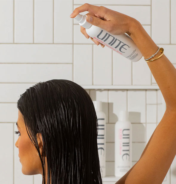 Model sprays Unite BOOSTA Volumizing Spray onto wet hair in front of a white tiled backdrop