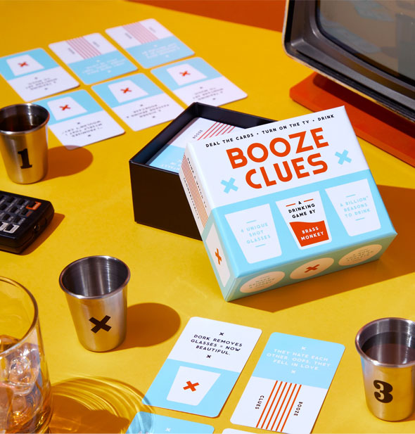 Booze Clues game box and components staged with retro TV and remote control on a yellow tabletop