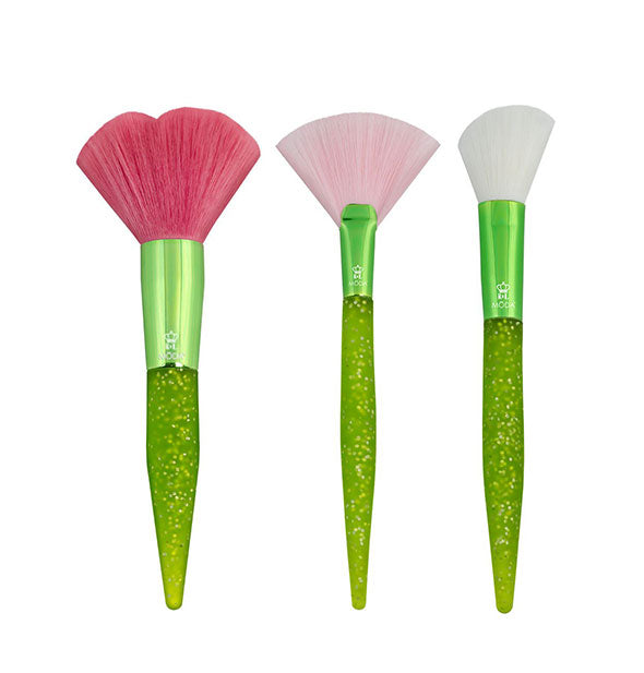 Three makeup brushes with green glitter handles, metallic green ferrules, and red, pink, and white fanned bristles respectively