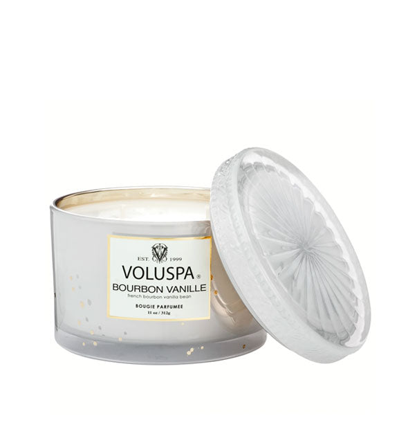 White glass Voluspa candle with speckled texture and gold accents shown with embossed glass lid set to the side