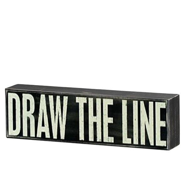 Black rectangular box sign with distressed finish says, "Draw the line" in large white lettering