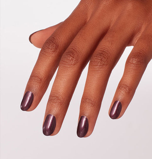 Model's hand wears a shimmery dark purple shade of nail polish