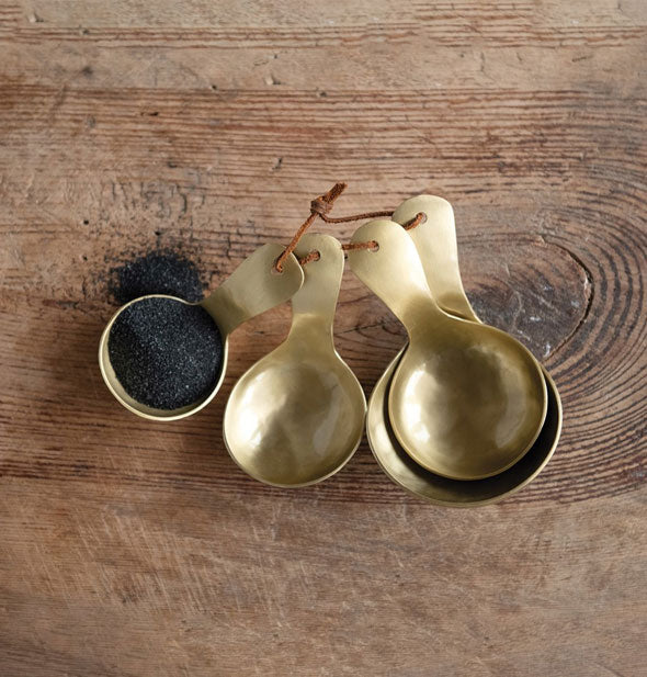 Set of four brass measuring spoons tied together with a piece of knotted brown leather sit on a wooden surface