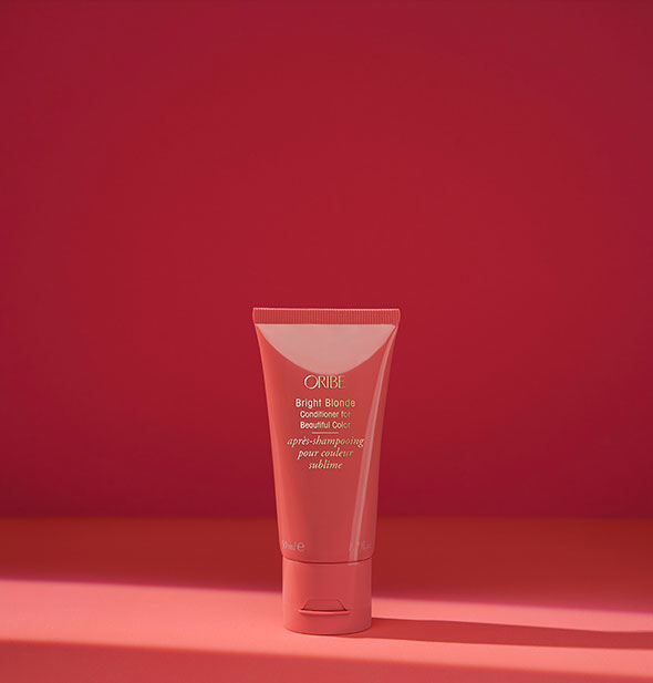 Small red bottle of Oribe Bright Blonde Conditioner for Beautiful Color on red background