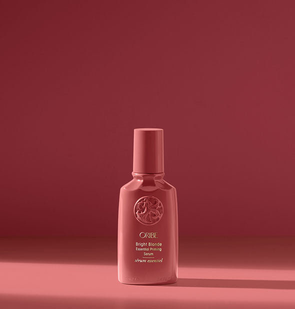 Dark pink bottle of Oribe Bright Blonde Essential Priming Serum on dark pink background