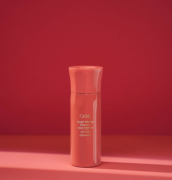 Small reddish bottle of Oribe Bright Blonde Radiance & Repair Treatment on red background