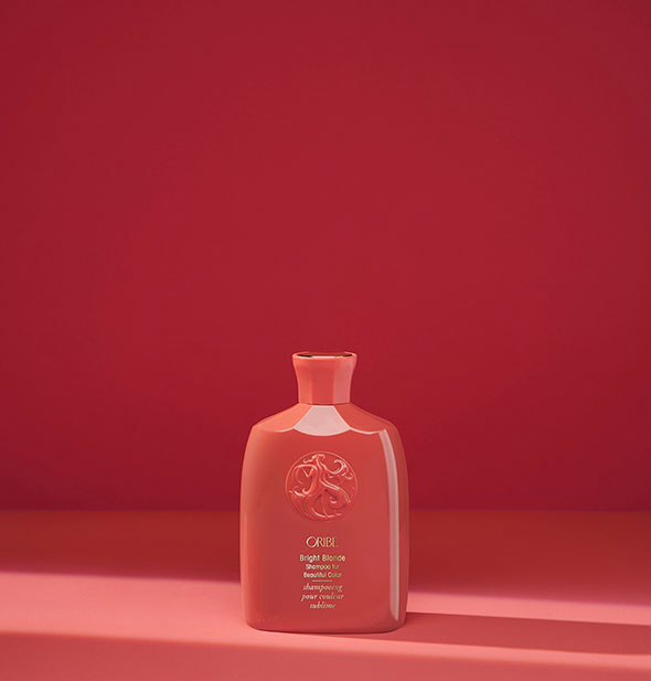 Small red bottle of Oribe Bright Blonde Shampoo for Beautiful Color on red background