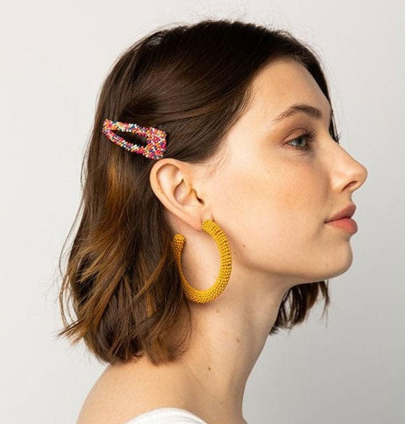 Model wears a colorful beaded hair clip in a swept-back style
