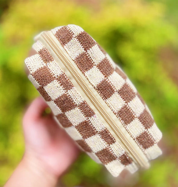 Model's hand holds a brown and white checker print knit makeup bag