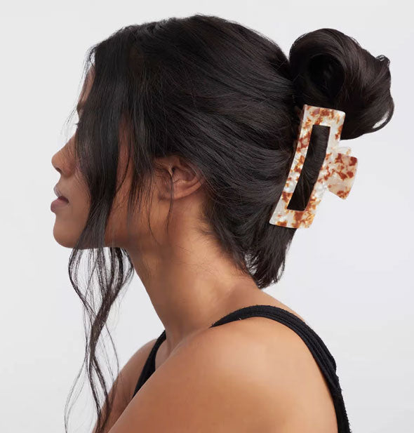 Model wears a brown and white marbled claw clip in an upswept style
