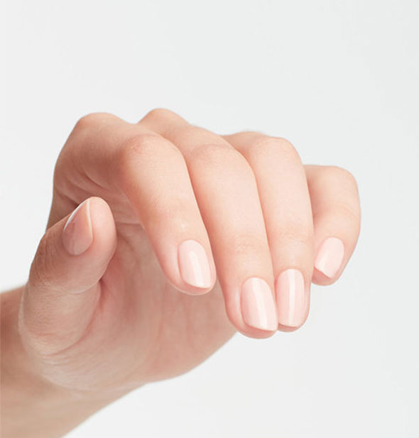 Model's hand wears a near-white pink shade of nail polish