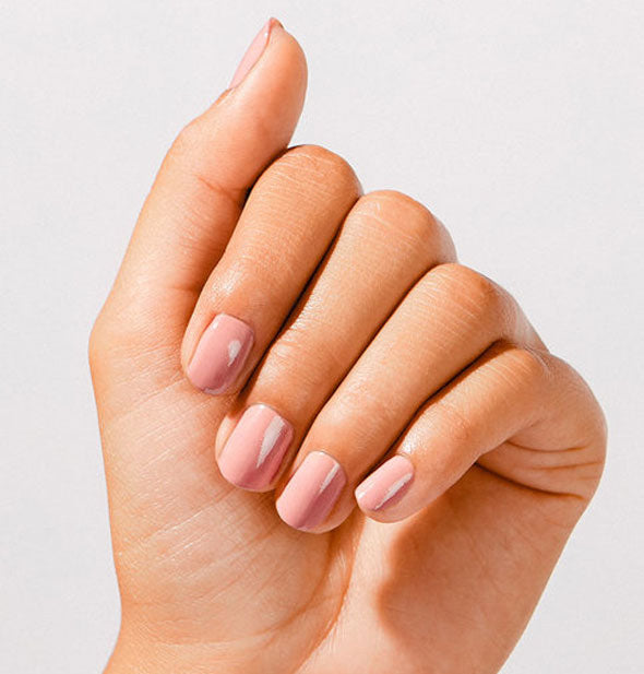 Model's hand wears a neutral pink shade of nail polish