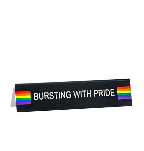 Black rectangular sign with rainbow designs says, "Bursting With Pride" in white lettering