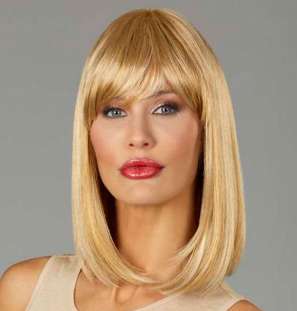 Model wearing a shoulder length, blonde wig with bangs.