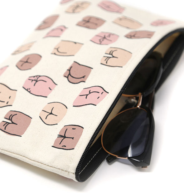 Canvas pouch with all-over buttocks illustrations and black zipper shown with a pair of sunglasses partially removed