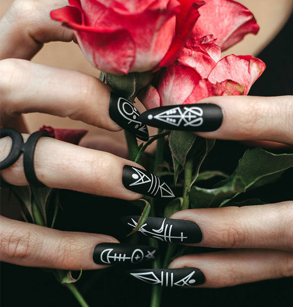 Hands wearing black and white graphic fingernails hold red roses