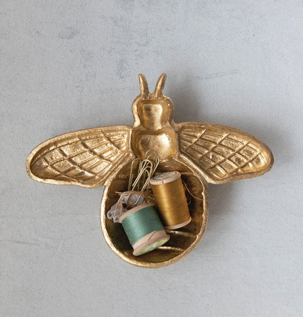Gold-toned cast iron bee-shaped dish holding some spools of thread and other small items