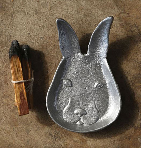 Cast iron dish shaped like a rabbit's head with partially burned wooden smudge stick to the side