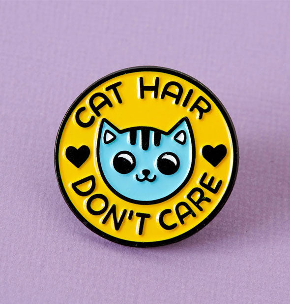 Round yellow enamel pin with blue kitty face says, "Cat Hair Don't Care" accented with black hearts