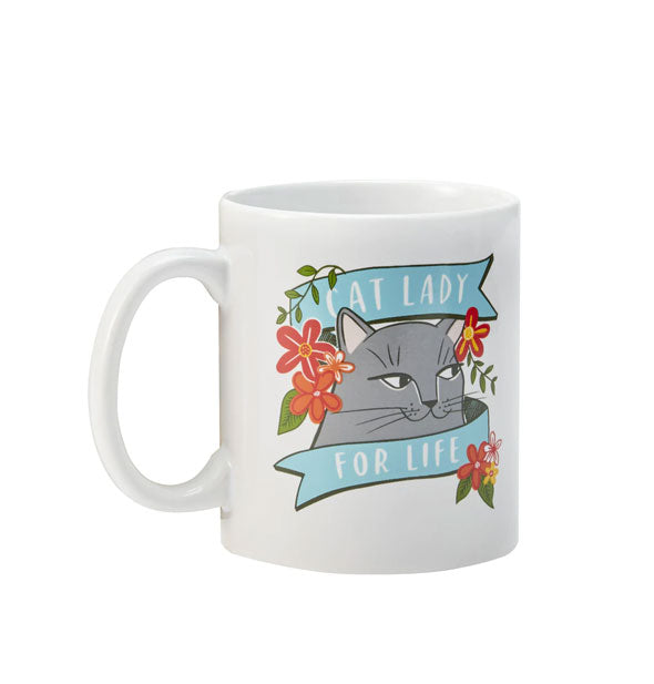 White coffee mug with illustration of a cat surrounded by orange flowers says, "Cat lady for life" in a blue banner