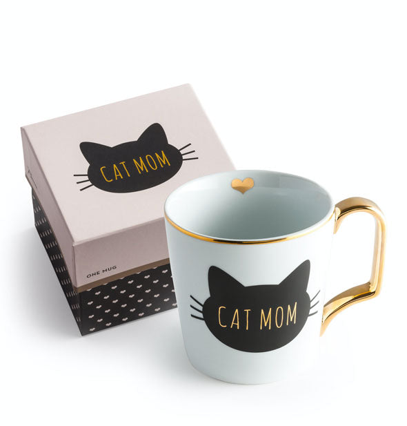 White mug with gold rim, inner heart detail, and handle features a black stylized cat head that says, "Cat Mom" in gold in the center; matching box sits behind
