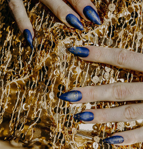 Hands wearing blue and gold celestial themed press on fingernails rest on a gold sequined background