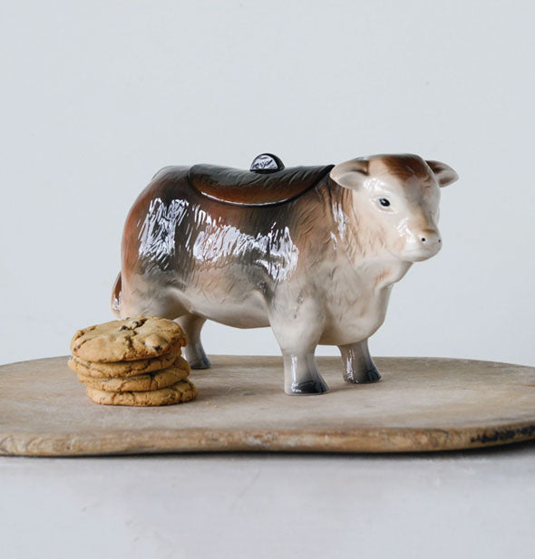 Ceramic cow cookie jar on a wooden platform with a small stack of chocolate chip cookies