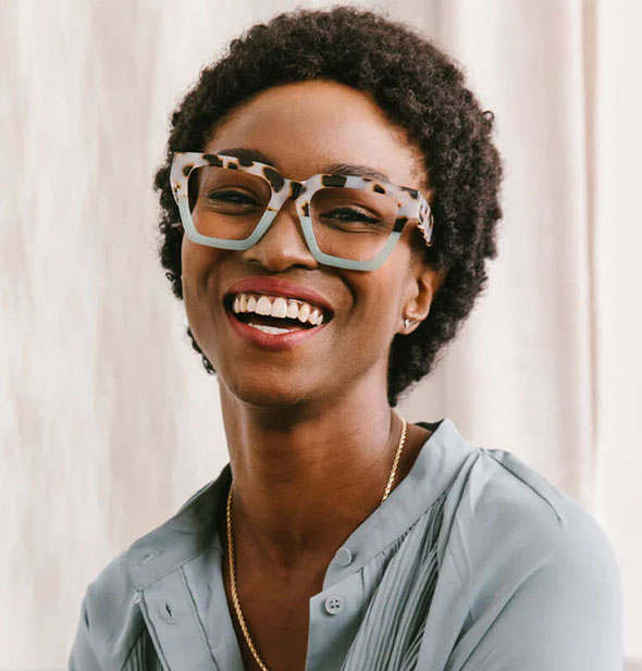 Smiling model wears a pair of square glasses frames with half green, half beige tortoise color blocked design