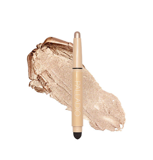 Double-ended Palladio eyeshadow stick with color at one end and black blending sponge at the other rests in front of a color swatch sample in the shade Champagne Shimmer