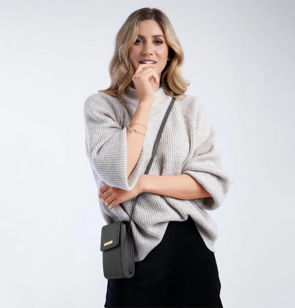 Model wears a small, dark gray crossbody purse 