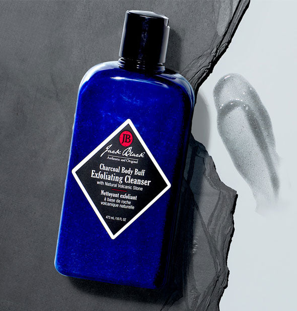 Jack Black Charcoal Body Buff Exfoliating Cleanser on slate surface with sample product application to the right on a lighter surface