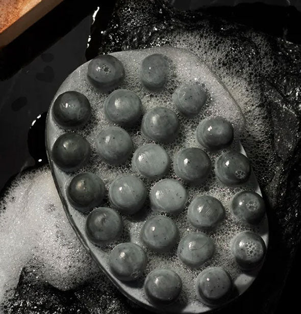 Underside of Jack Black Charcoal Body Bar with massaging nubs shown covered in soapy lather