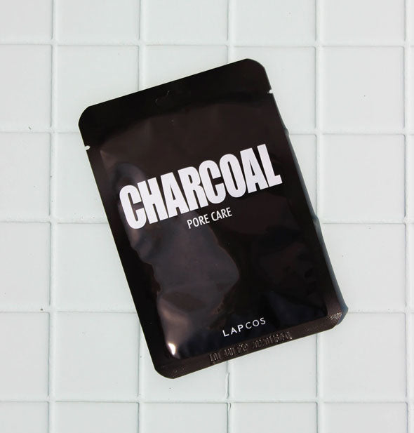 Black LAPCOS Charcoal Pore Care mask packet rests on a white tile surface