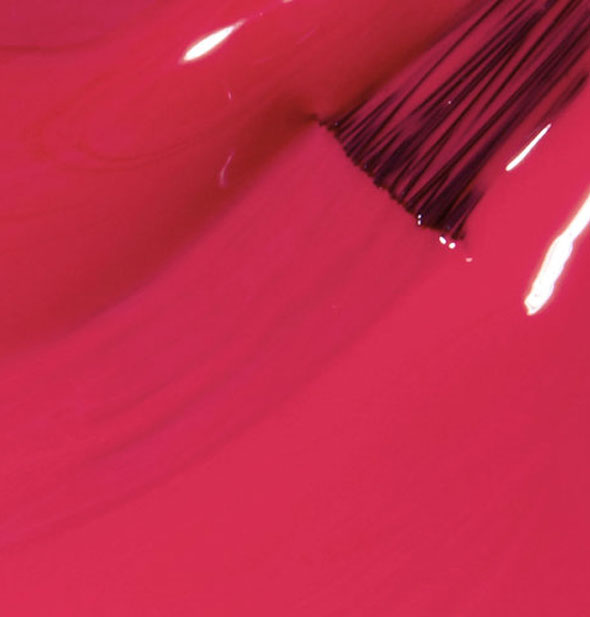 Closeup of deep pink nail polish with brush tip drawn through it
