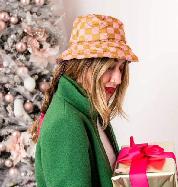 Model holding a gift wears a brown and pink checker print quilted bucket hat