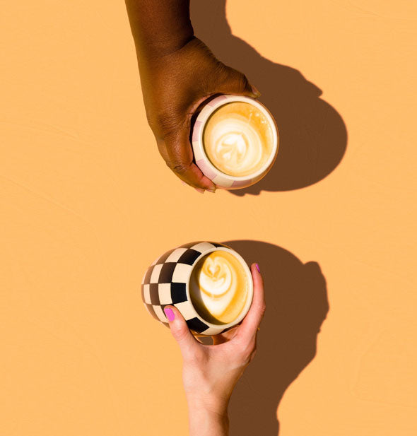 Two models' hands hold checkerboard print mugs filled with lattes