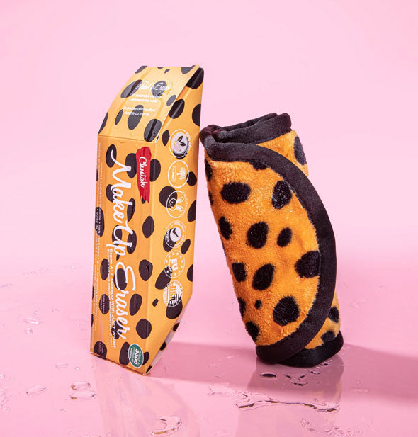 Rolled up Cheetah MakeUp Eraser leans against box on a pink surface sprinkled with water