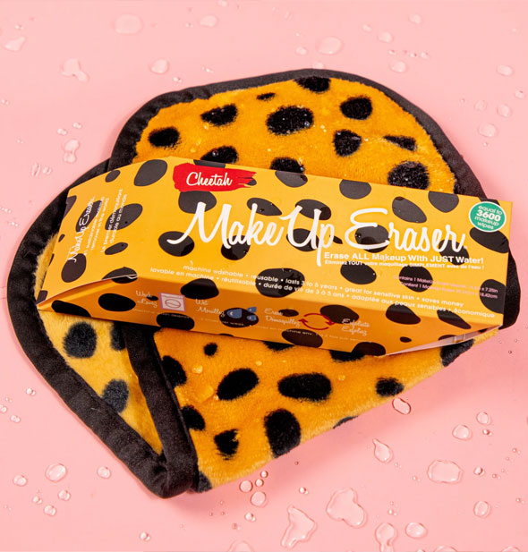 Cheetah MakeUp Eraser with box resting on top of it on a pink surface sprinkled with water droplets