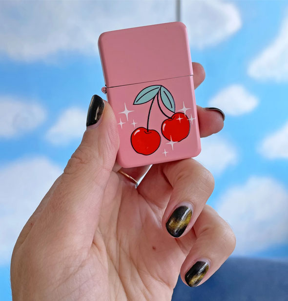 Model's hand holds the cherries lighter for size reference against a cloud print backdrop